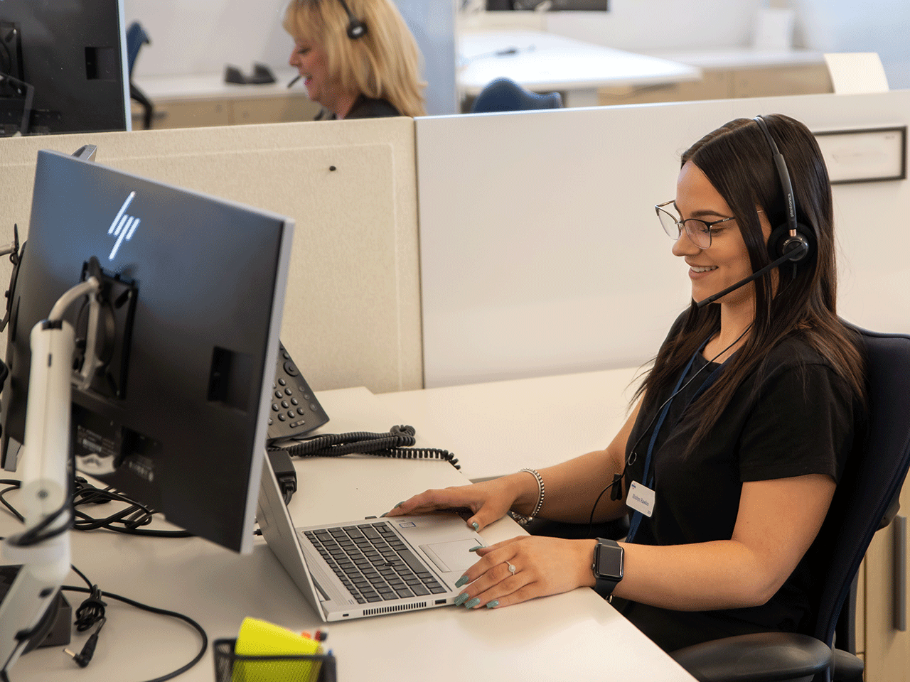 A woman sitting on a chair in front of a desktop with headphones on and her hands are resting on a table.