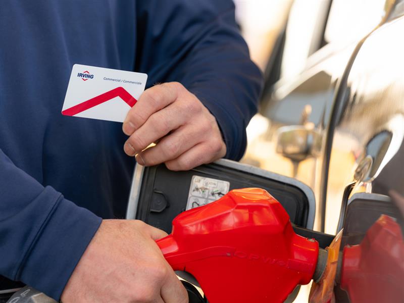 A man filing up his car at the gas station with Irving commercial card in his left hand and fuel nozzle in right hand.